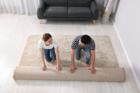 Smiling couple unrolling carpet on floor in roomの写真素材