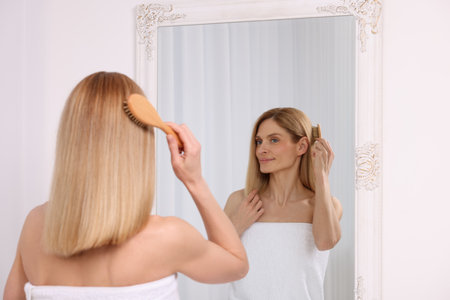 Beautiful woman brushing her hair near mirror in roomの写真素材
