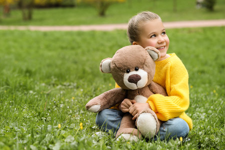 Little girl with teddy bear on green grass outdoors. Space for textの写真素材