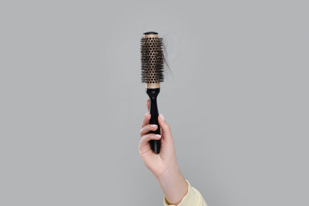 Woman holding brush with lost hair on gray background, closeup. Alopecia problemの写真素材