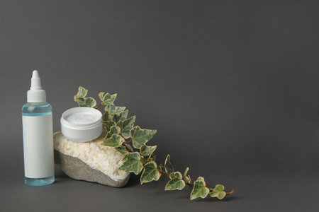 Cosmetic products, stone and ivy leaves on dark gray background. Space for textの写真素材
