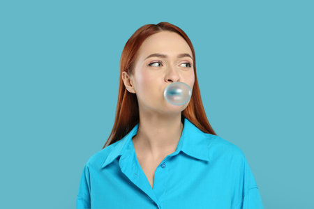 Beautiful woman blowing bubble gum on turquoise backgroundの写真素材