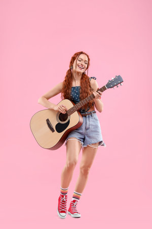 Stylish young hippie woman playing guitar on pink backgroundの写真素材