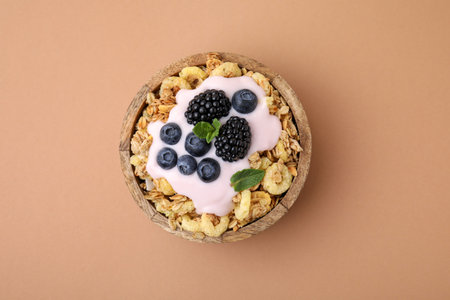 Tasty granola, yogurt and fresh berries in bowl on pale brown background, top view. Healthy...