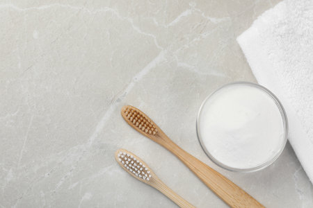 Bamboo toothbrushes, glass bowl of baking soda and towel on light gray marble table, flat lay. Space...