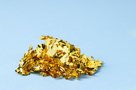 Many pieces of edible gold leaf on light blue background, closeup