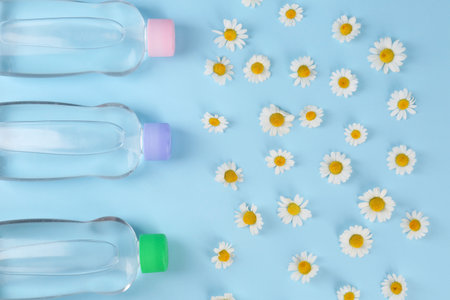 Bottles with baby oil and daisies on light blue background, flat layの写真素材