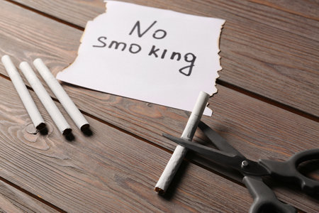 Words No Smoking written on paper and scissors cutting cigarette on wooden tableの写真素材