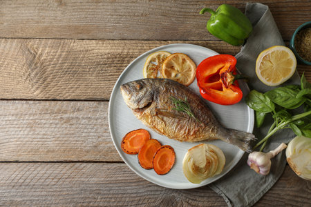 Delicious dorado fish with vegetables and herbs served on wooden table, flat lay. Space for textの写真素材