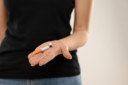 Stop smoking concept. Woman holding broken cigarette on beige background, closeup. Space for textの写真素材