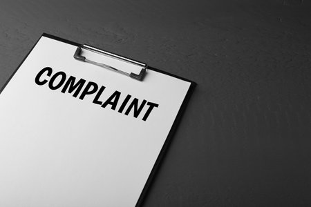 Paper with word Complaints attached to clipboard on black background. Space for textの写真素材