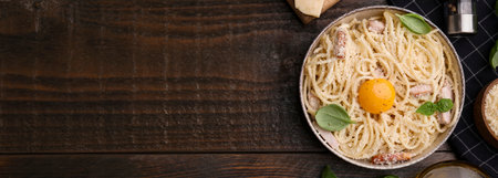 Bowl of tasty pasta Carbonara with basil leaves and egg yolk on wooden table, flat lay. Banner design with space for textの写真素材