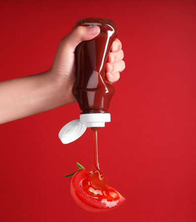 Woman squeezing organic ketchup onto cut tomato against red background, closeupの写真素材