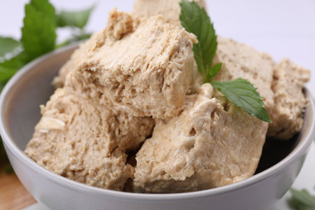 Bowl with pieces of tasty halva and mint leaves in bowl, closeup