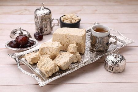 Pieces of tasty halva, tea and dates on light wooden tableの写真素材