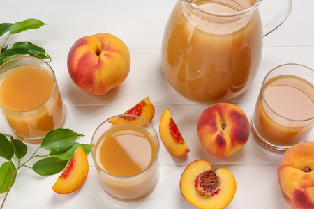Delicious peach juice, fresh fruits and leaves on white wooden tableの写真素材