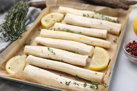 Baking tray with raw salsify roots, lemon and thyme on white marble table, closeupの写真素材