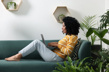Relaxing atmosphere. Woman with laptop on sofa near houseplants in roomの写真素材