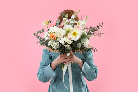 Woman covering her face with bouquet of beautiful flowers on pink backgroundの写真素材