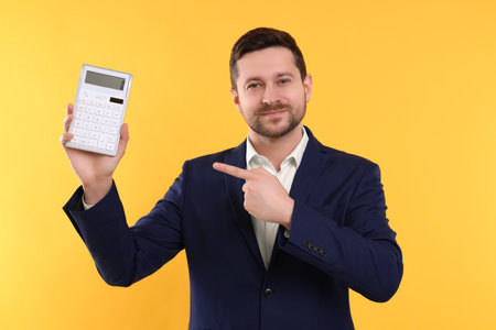 Happy accountant showing calculator on yellow backgroundの写真素材