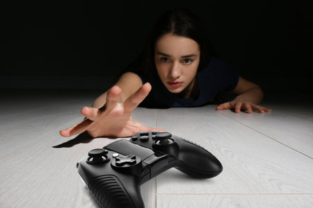 Gaming disorder. Woman reaching out for gamepad on floor from darknessの写真素材