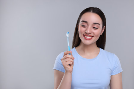 Happy young woman holding plastic toothbrush on light gray background, space for textの写真素材