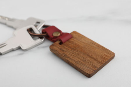 Keys and wooden keychain with Ukrainian coat of arms on white marble table, closeup