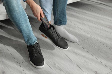 Man putting orthopedic insole into shoe indoors, closeup. Space for text