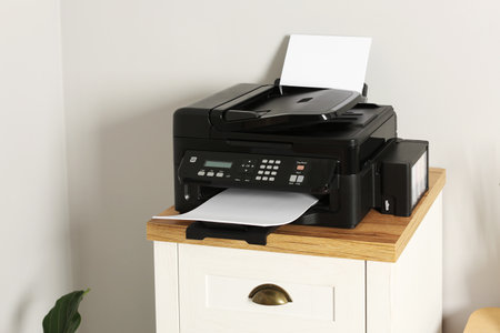 Modern printer with paper on chest of drawers indoors
