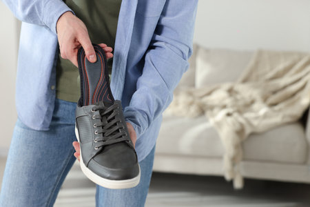 Man putting orthopedic insole into shoe indoors, closeup. Space for text
