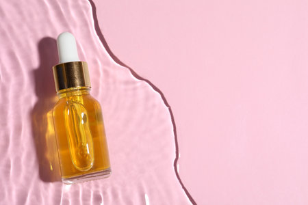 Bottle of cosmetic oil in water on pink background, top view. Space for textの写真素材