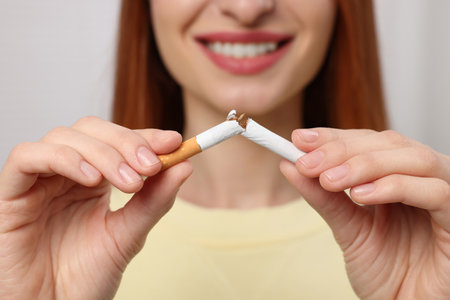 Stop smoking concept. Woman breaking cigarette on light gray background, closeupの写真素材