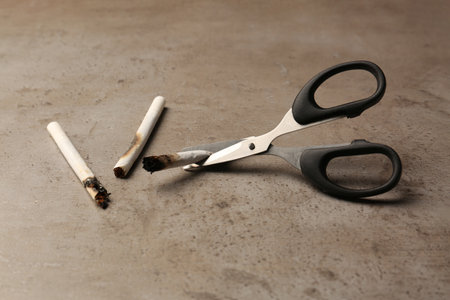 Scissors cutting burnt cigarettes on gray textured table. No smoking concept