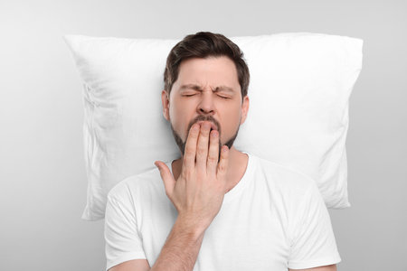 Tired man with pillow on light gray background. Insomnia problemの写真素材
