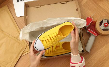 Woman packing sneakers into cardboard box at wooden table, top view. Online storeの写真素材