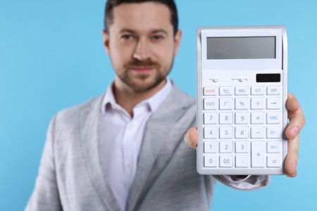 Happy accountant with calculator on light blue background, selective focusの写真素材