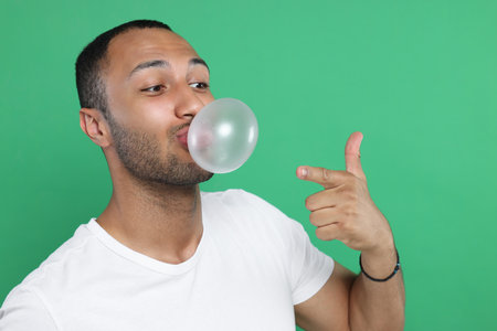 Man blowing bubble gum on green background. Space for textの写真素材