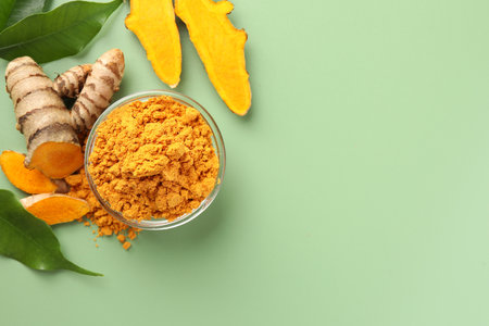 Aromatic turmeric powder, raw roots and leaves on green background, flat lay. Space for textの写真素材