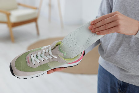 Woman putting orthopedic insole into shoe at home, closeup. Foot care