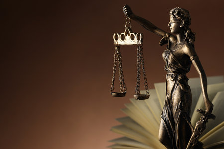 Statue of Lady Justice near book on brown background, space for text. Symbol of fair treatment under lawの写真素材