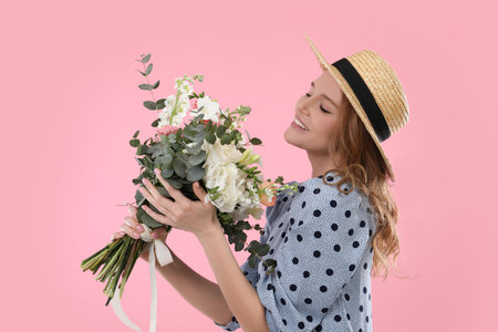 Beautiful woman in straw hat with bouquet of flowers on pink backgroundの写真素材