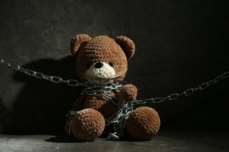 Stop child abuse. Chained toy bear on dark gray backgroundの写真素材