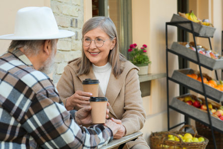 Affectionate senior couple sitting in outdoor cafe and drinking coffee, space for textの写真素材