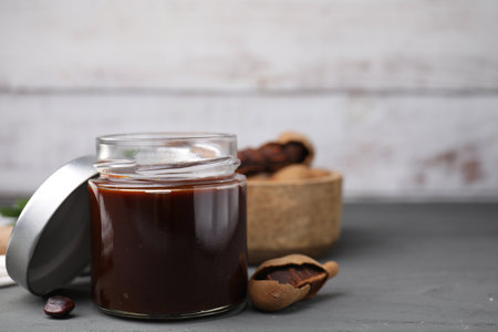 Jar of tasty tamarind sauce and fresh pods on gray wooden table. Space for textの写真素材