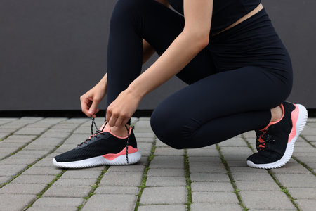 Woman tying shoelace of sneakers on street, closeup