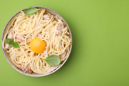 Bowl of tasty pasta Carbonara with basil leaves on light green background, top view. Space for textの写真素材