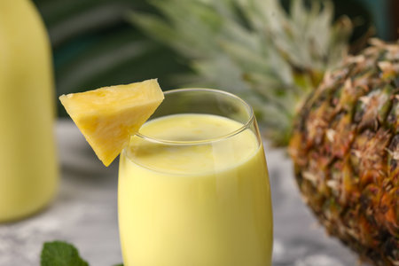 Tasty pineapple smoothie in glass and fruit on table, closeup