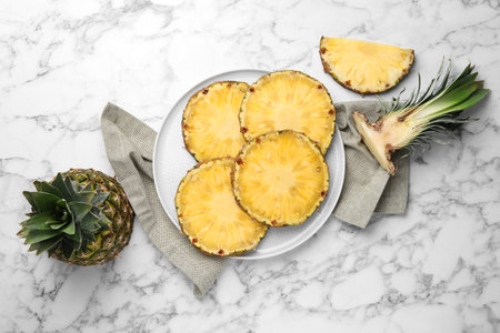 Slices of tasty ripe pineapple and whole fruit on white marble table, flat layの写真素材