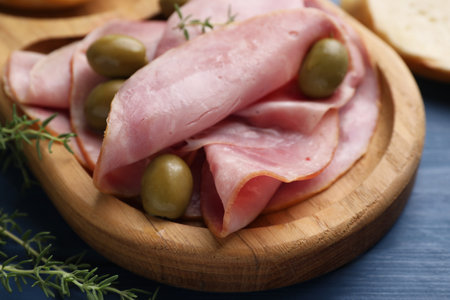 Slices of delicious ham with olives and thyme on blue wooden table, closeupの写真素材