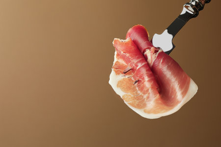 Fork with slice of tasty jamon on brown background, closeup. Space for textの写真素材